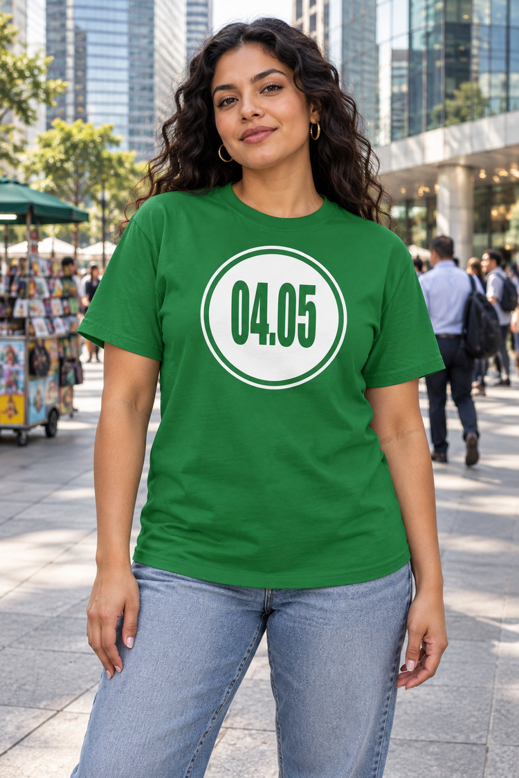 AI-generated Latina woman age 26, olive skin, medium curvy build, long curly dark hair behind shoulders wearing Women’s 04.05 Bordered Circle Classic Tee — Turf Green; busy downtown plaza with commuters, street vendors and glass towers