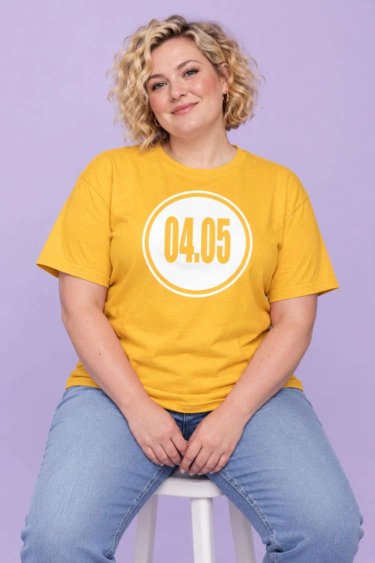 AI-generated White woman age 33, fair skin, plus-size build, short blonde curly hair wearing Women’s 04.05 Bordered Circle Classic Tee — Daisy; clean pale lavender studio