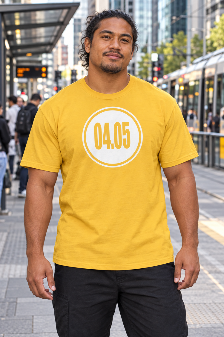 AI-generated Pacific Islander man age 28, warm brown skin, muscular broad build, long wavy hair tied back wearing Men’s 04.05 Bordered Circle Classic Tee — Daisy; busy downtown tram stop with commuters and city traffic