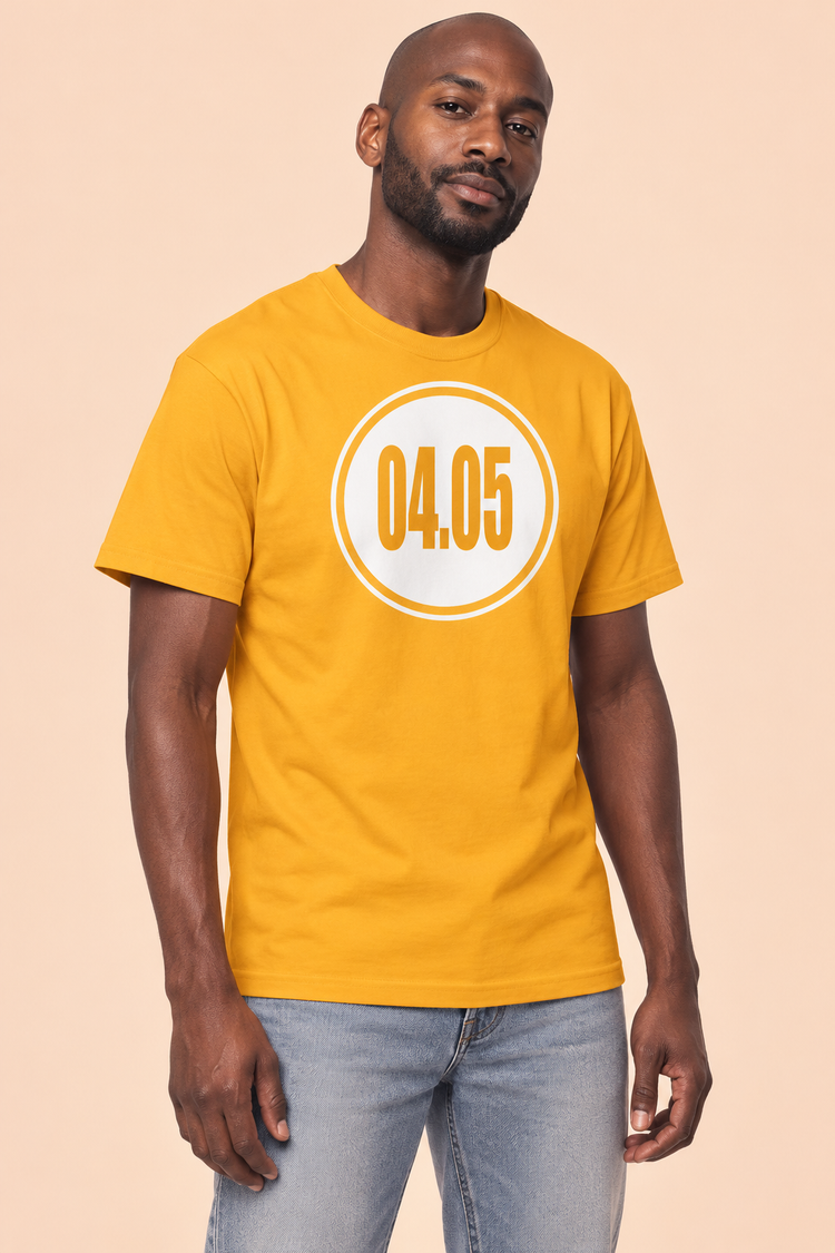AI-generated Black man age 36, deep brown skin, slim build, shaved head and short beard wearing Men’s 04.05 Bordered Circle Classic Tee — Gold; clean pale peach studio
