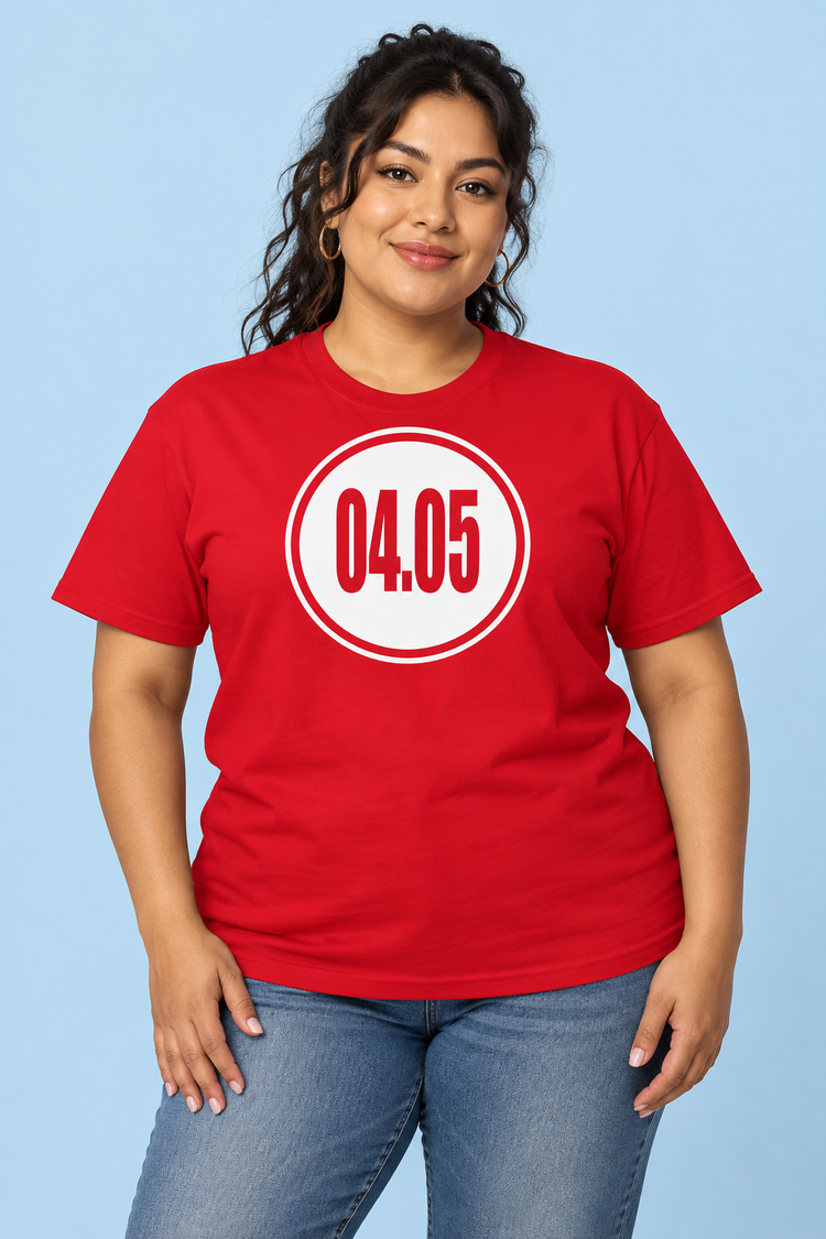 AI-generated Latina woman age 35, medium tan skin, plus-size build, dark wavy hair swept back wearing Women’s 04.05 Bordered Circle Classic Tee — Red; clean pale blue studio
